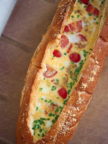 baked eggs with tomatoes, chives, and cheese inside of a loaf of bread.
