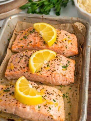 three salmon fillets with lemon wedges on top.