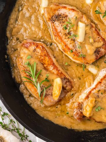 pan seared pork chops with gravy in a cast iron skillet.