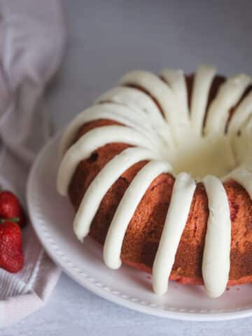 An entire cake on a white plate with fresh strawberries on the side.