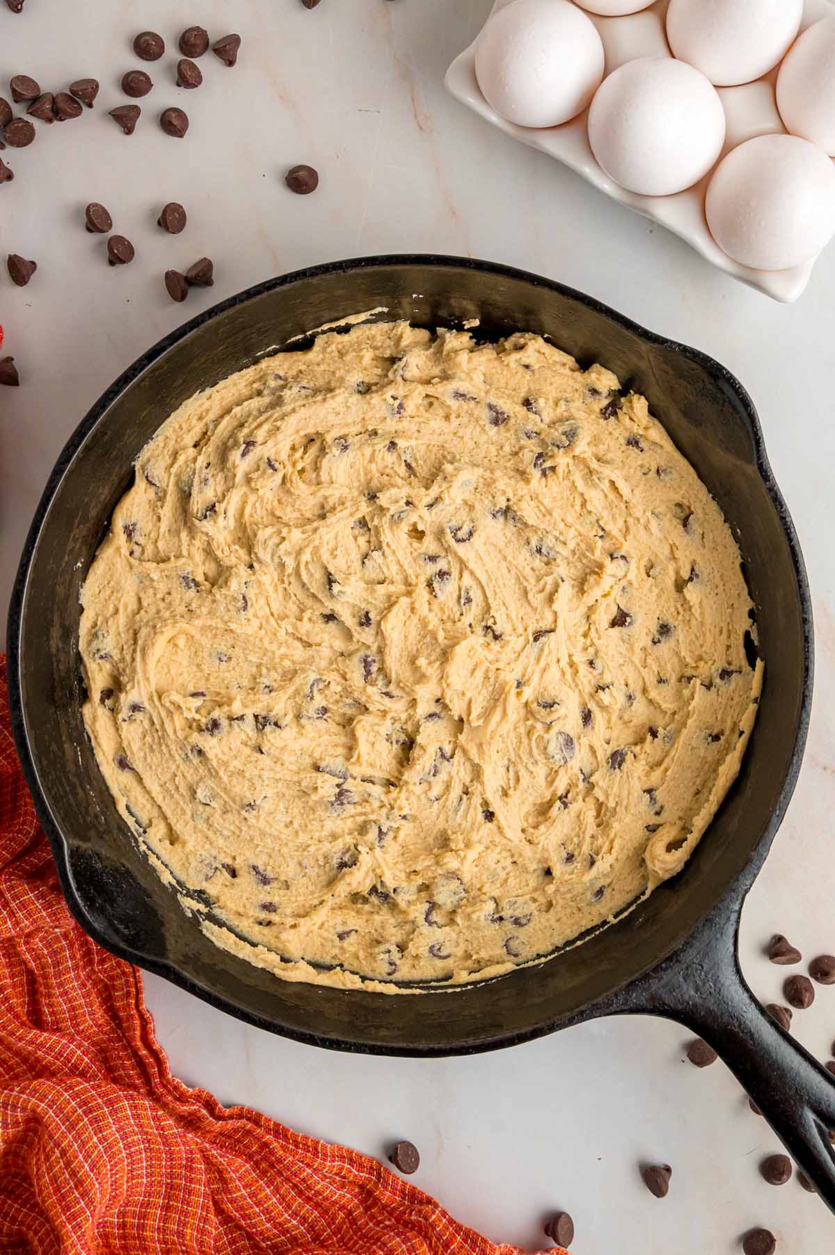 Cookie dough in a 10-inch iron skillet with eggs and chocolate chips on the side.