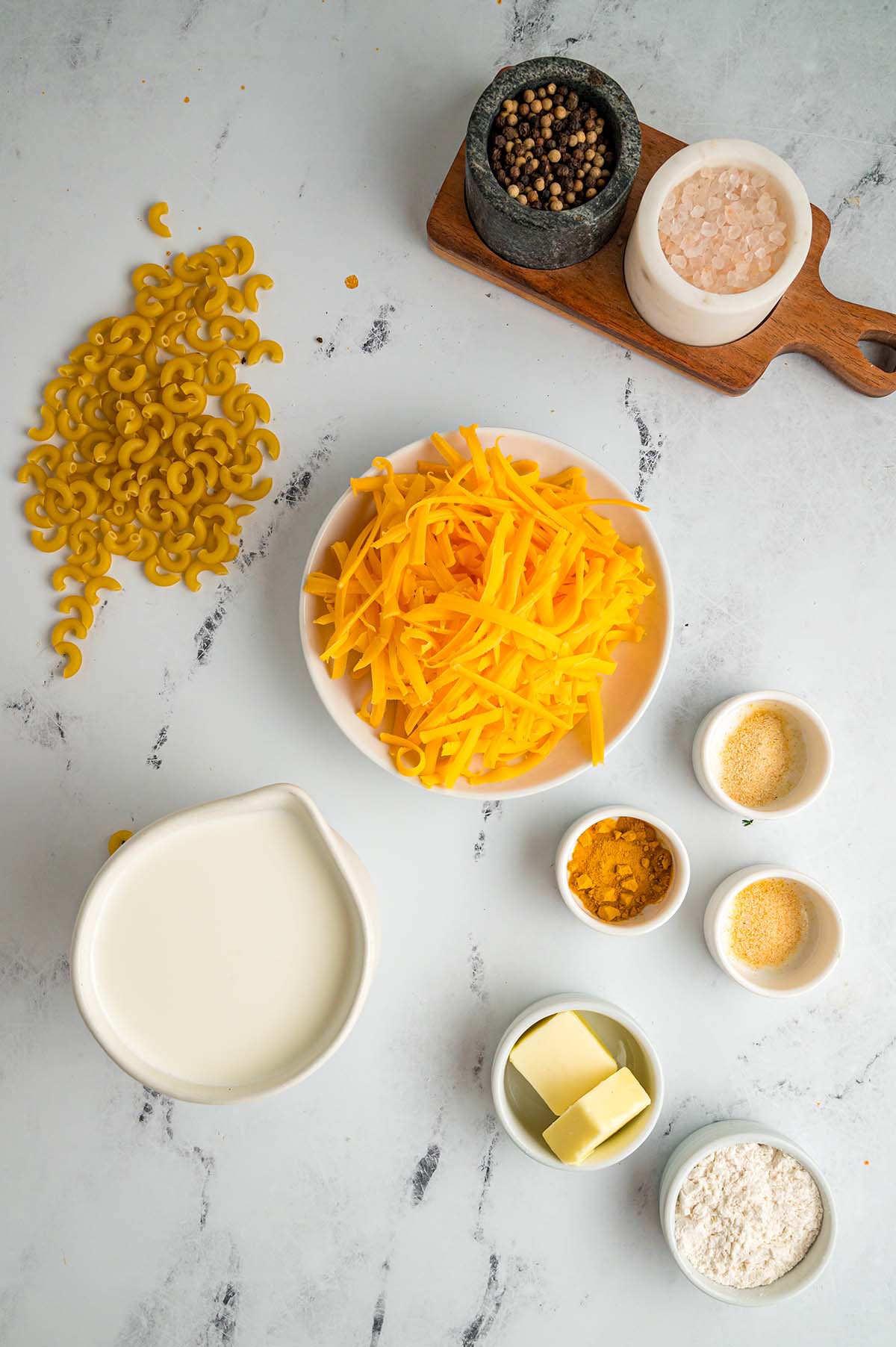 cheese, macaroni, half and half, butter, spices, and flour on a white surface. 