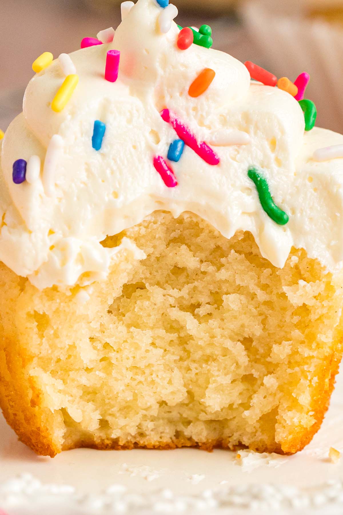 A bitten vanilla cupcake with frosting up close. 