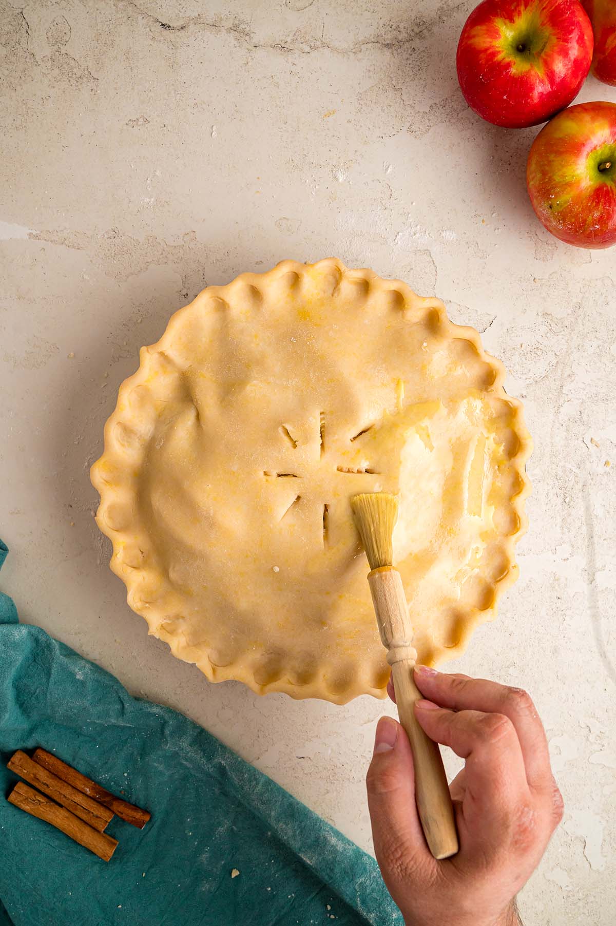 A pastry brush brushing the apple pie with egg wash.