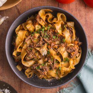 Short rib pasta in a bowl with tomatoes, onions, and garlic on the side.
