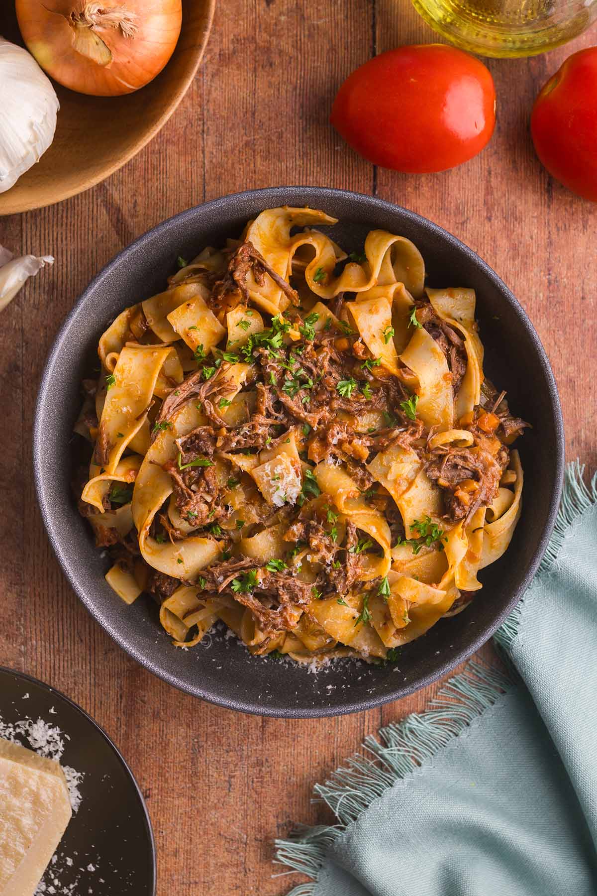 Short rib pasta in a bowl with tomatoes, onions, and garlic on the side.