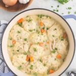 A pot filled with chicken and dumplings with onions, parsley, and garlic on the side.