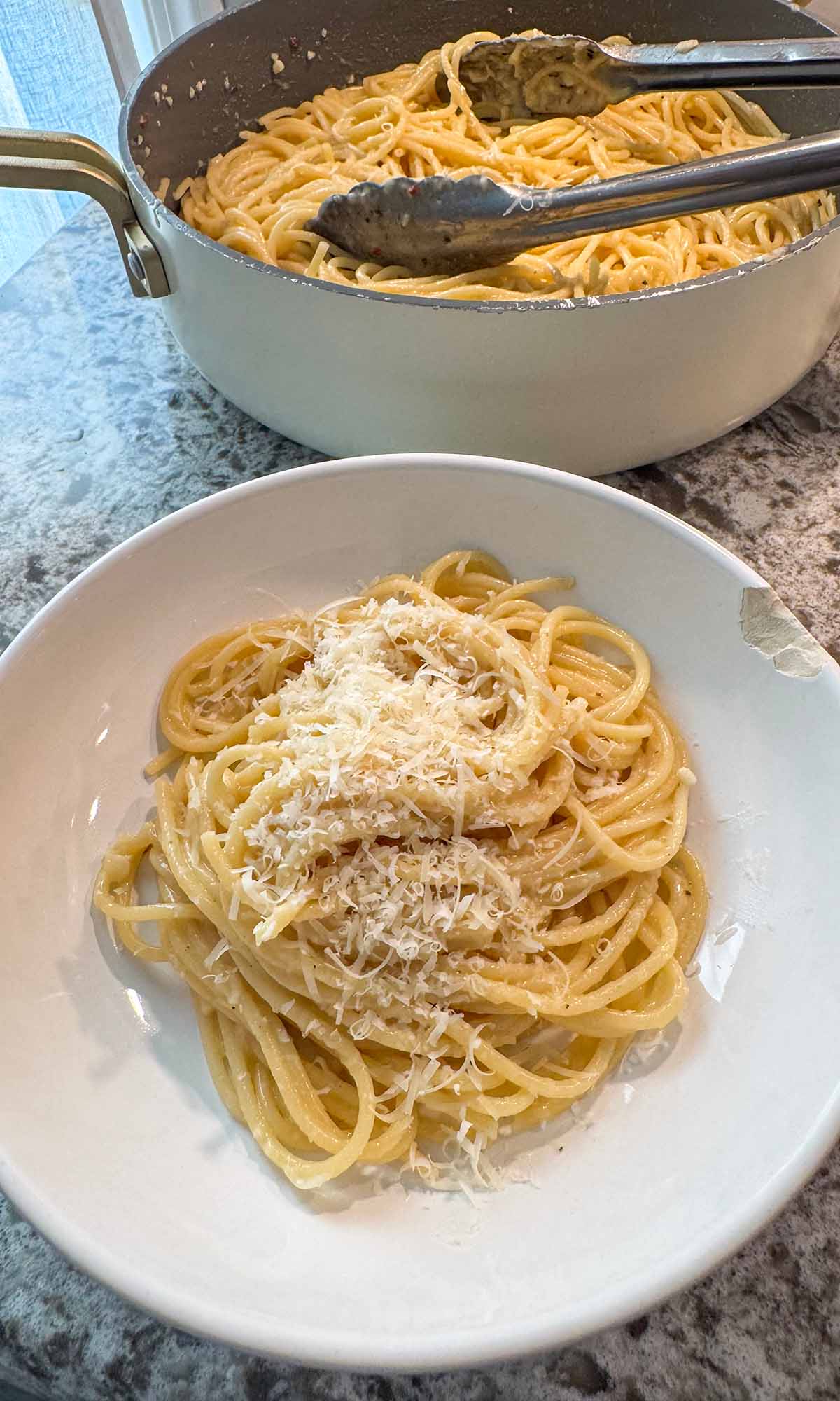 Buttered noodles in a bowl and a skillet in the background.