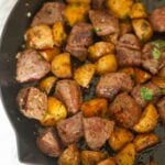 Steak bites and potato cubes in a skillet.