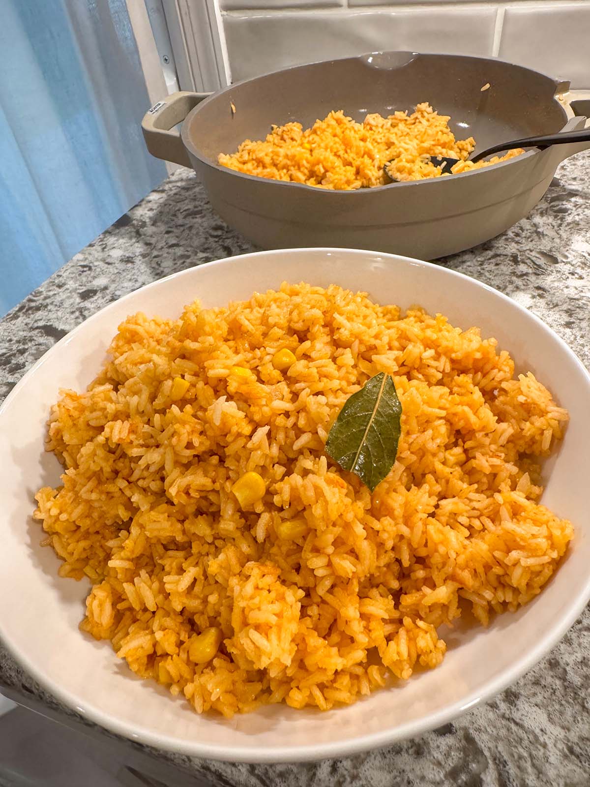 A white bowl filled with Mexican rice and a pot of Mexican rice in the background.