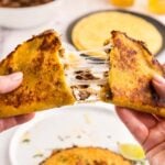 A hand holding up a birria taco with cheese.