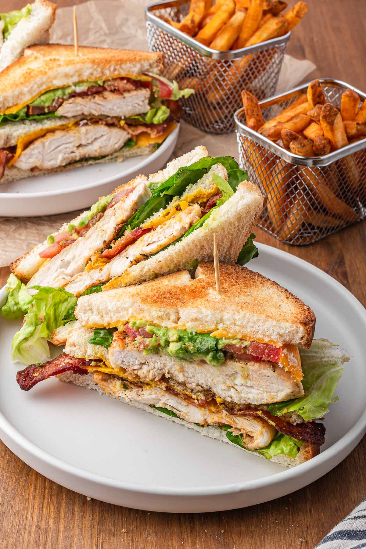 A chicken club sandwich with French fries on the side. 