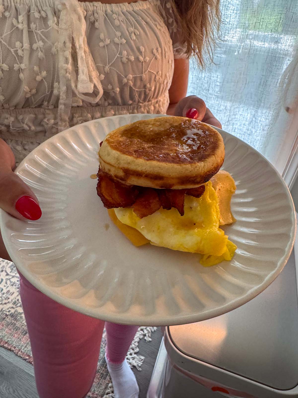 A person holding a McGriddle sandwich on a white plate.
