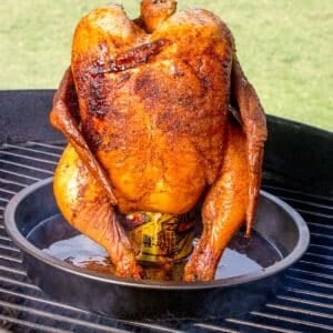 A whole chicken cooked upright on a beer can on the grill.