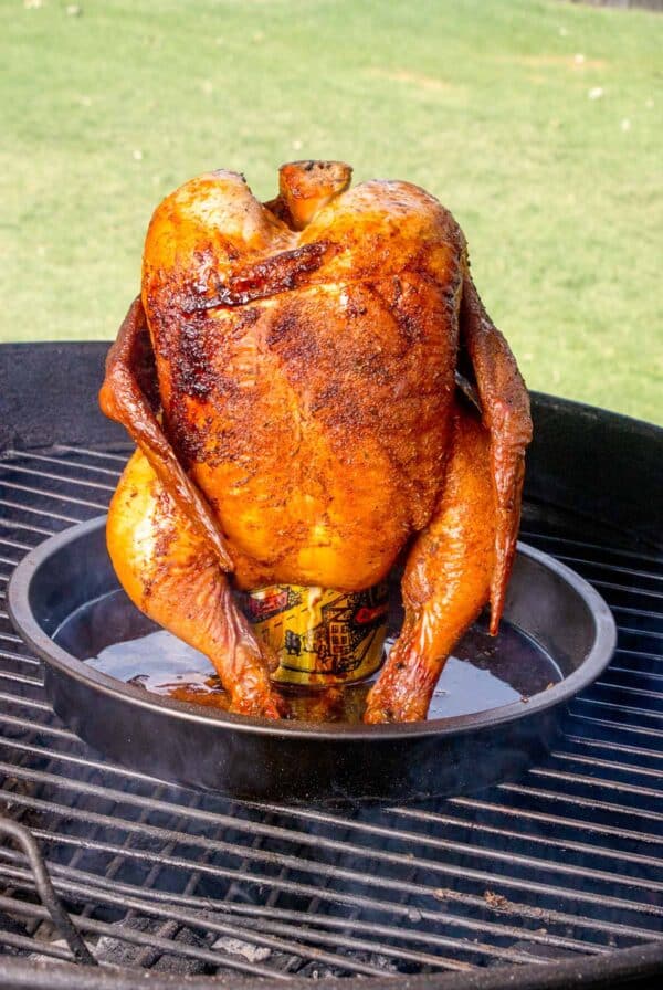 A whole chicken cooked upright on a beer can on the grill.