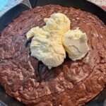 Chocolate brownie skillet with three scoops of vanilla ice cream on top.