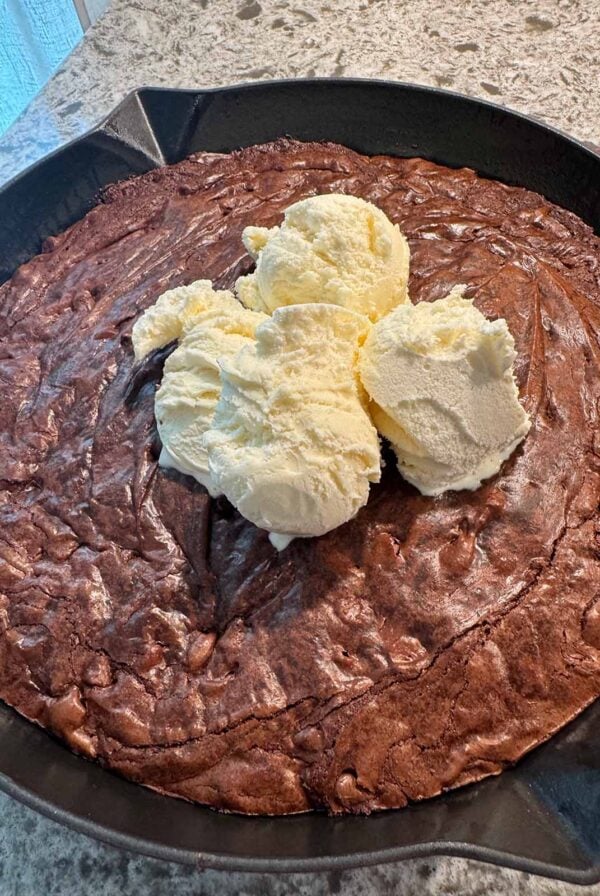 Chocolate brownie skillet with three scoops of vanilla ice cream on top.