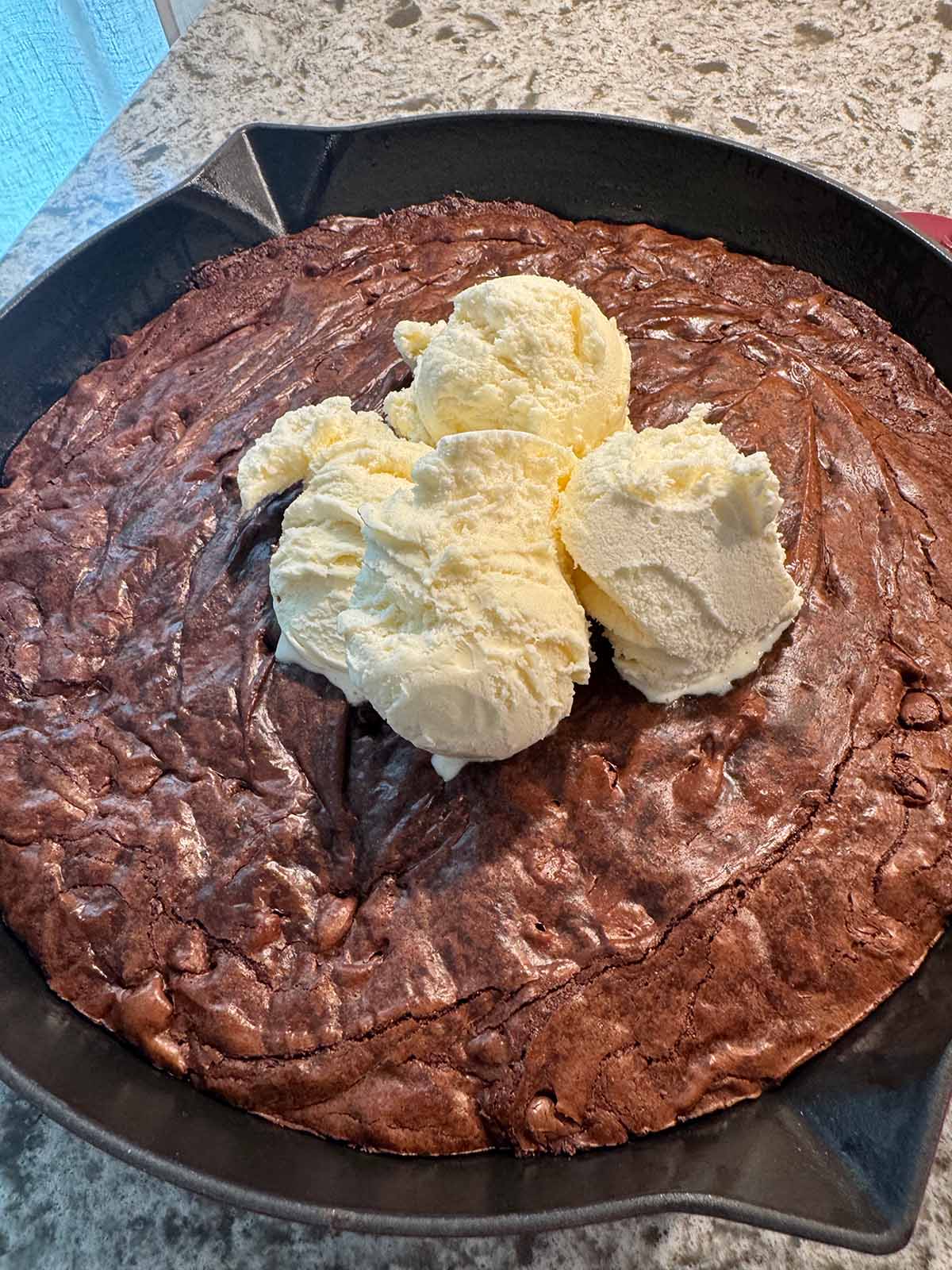 Chocolate brownie skillet with three scoops of vanilla ice cream on top. 