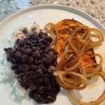grilled chicken with onions on top with a side of rice and black beans.