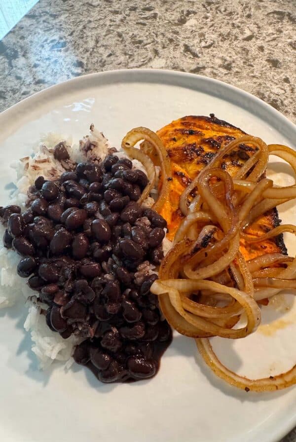 grilled chicken with onions on top with a side of rice and black beans.