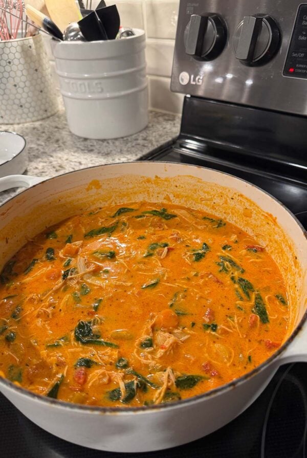 Marry me chicken noodle soup cooking on the stovetop in a white dutch oven.