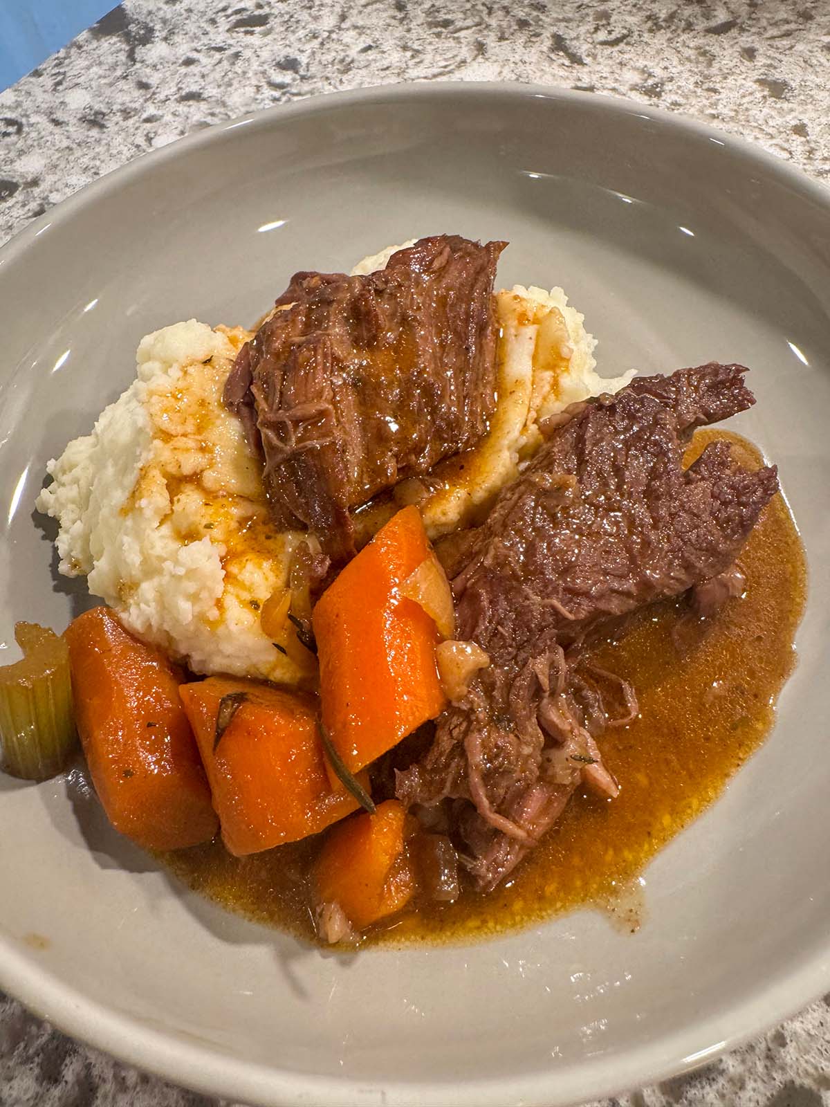 Pot roast with mashed potatoes, carrots, celery, and gravy.