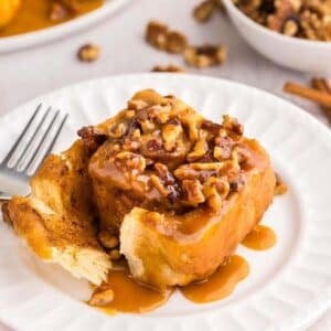 One sticky bun on a white plate with a fork.