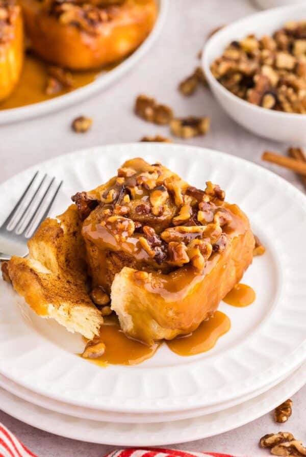 One sticky bun on a white plate with a fork.