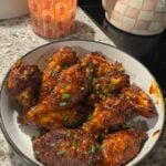 Cooked and sauced wings in a white bowl with a candle and tea kettle in the background.