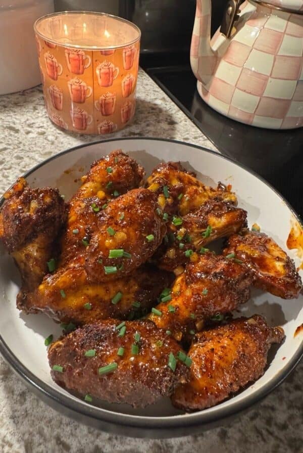 Cooked and sauced wings in a white bowl with a candle and tea kettle in the background.