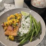 Cooked salmon topped with mango salsa, served with rice, asparagus, and a lime wedge.
