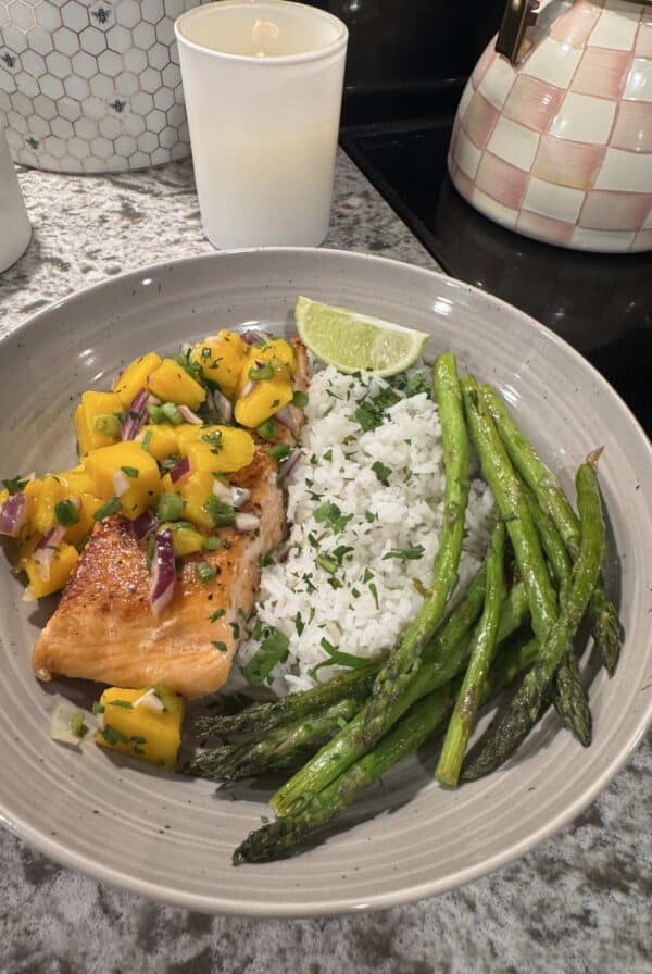 Cooked salmon topped with mango salsa, served with rice, asparagus, and a lime wedge.