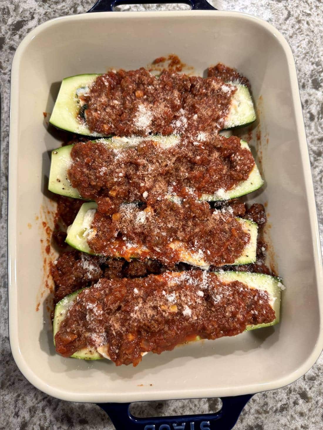 four zucchinis with meat sauce and parmesan cheese on top.