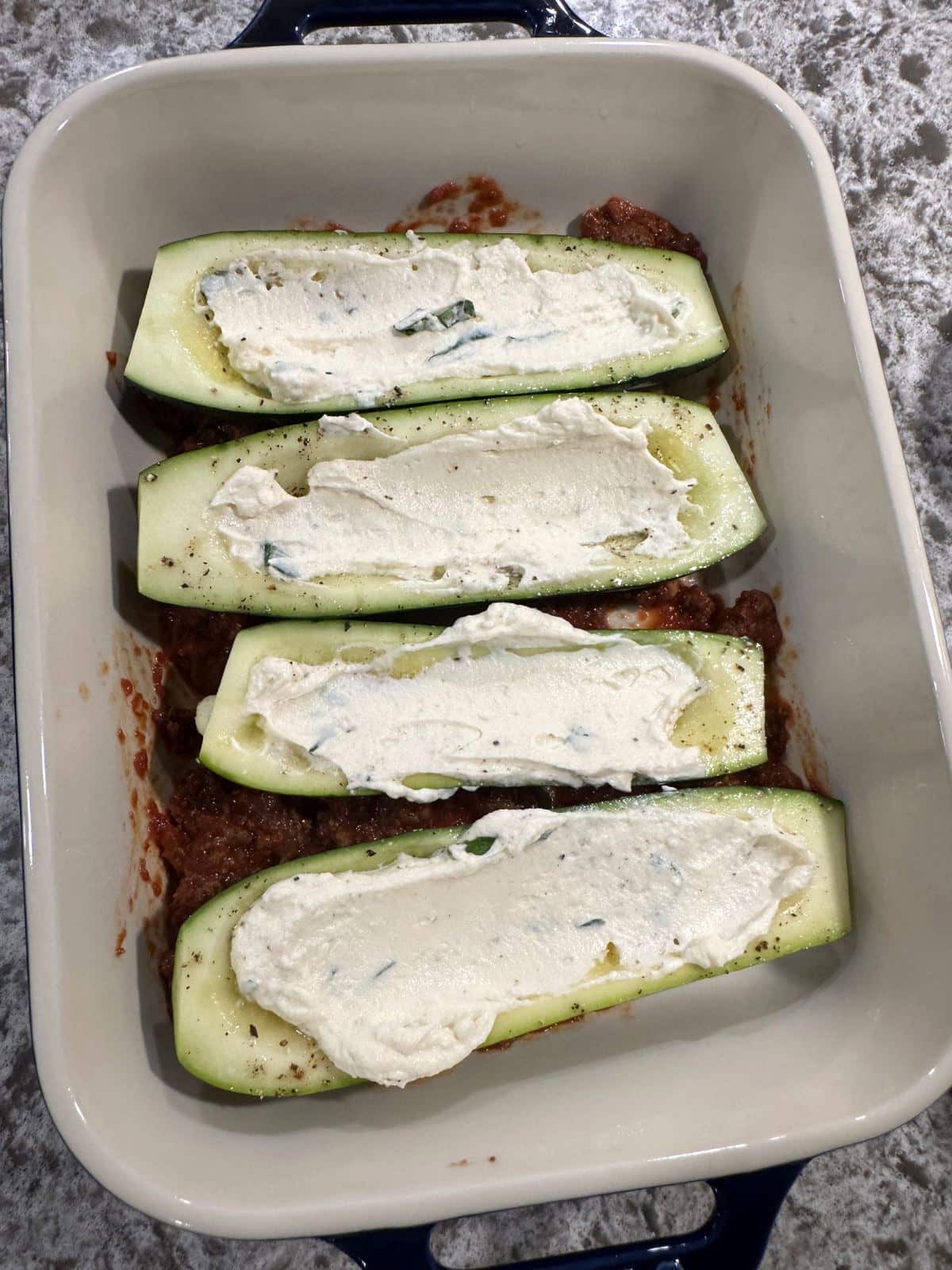 Four zucchini boats with ricotta filling and meat sauce underneath.