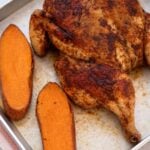 Cooked spatchcock chicken with roasted sweet potatoes on a sheet pan.