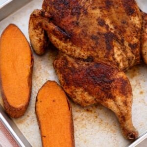 Cooked spatchcock chicken with roasted sweet potatoes on a sheet pan.