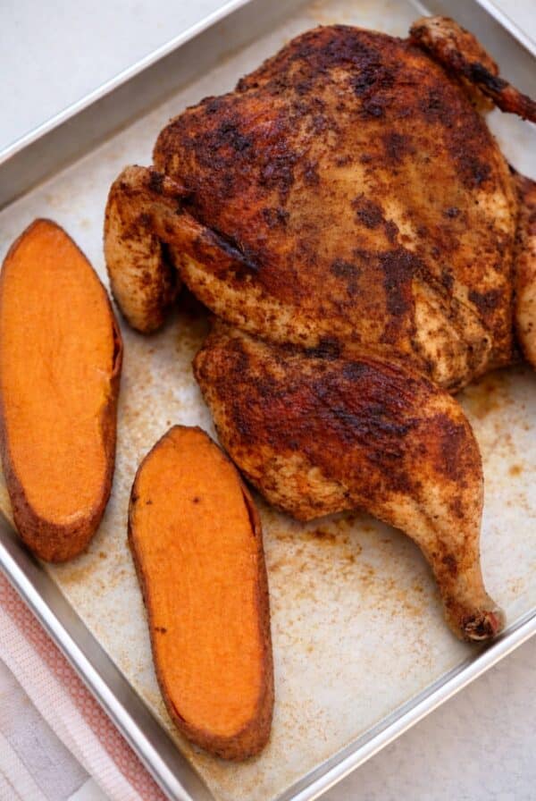 Cooked spatchcock chicken with roasted sweet potatoes on a sheet pan.