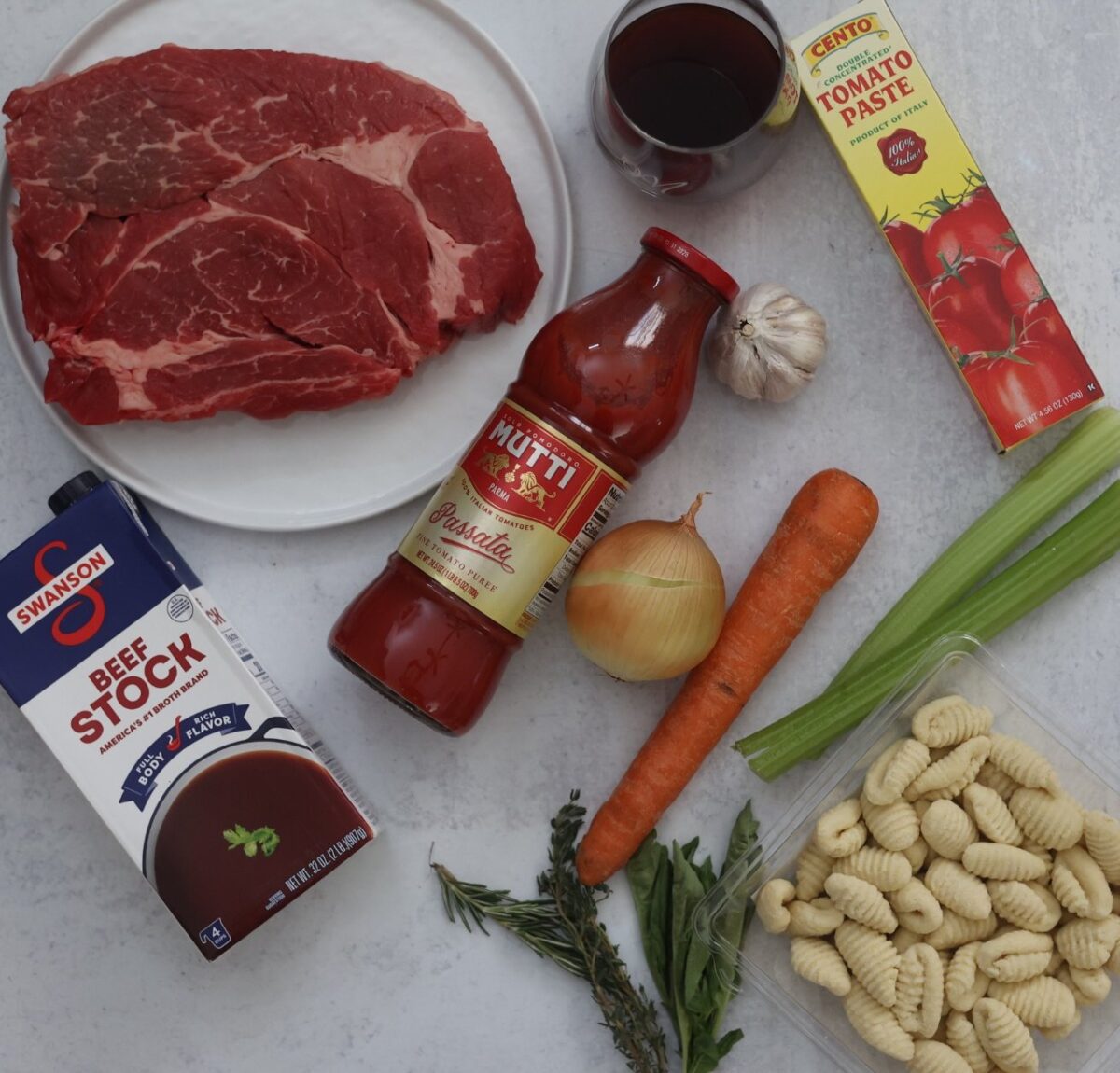 Braised beef gnocchi ingredients: chuck roast, tomato sauce, stock, wine, veggies, herbs, and gnocchi.