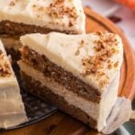 Layered carrot cake cheesecake with cream cheese frosting and chopped pecans on a wooden cake stand.