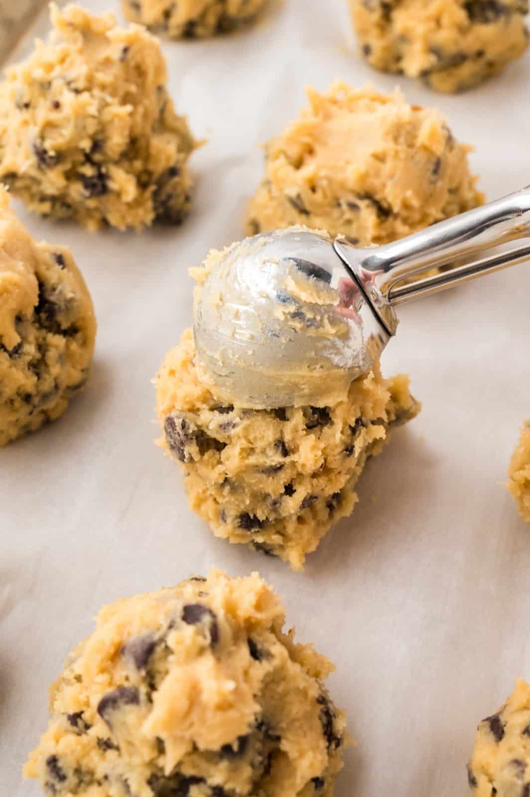 Scooping chocolate chip cookie dough onto a parchment lined baking sheet.