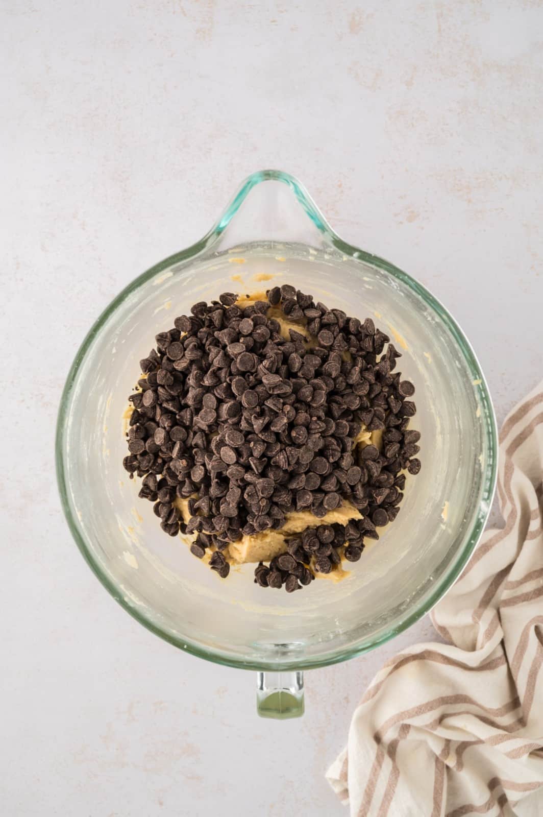 Chocolate chips added to cookie dough in a glass mixing bowl.