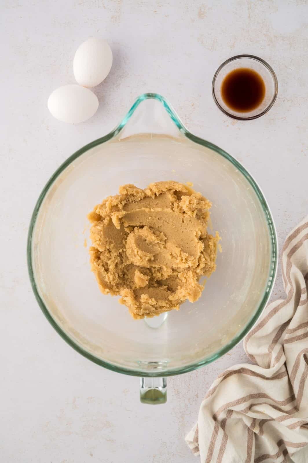 Cookie dough being mixed in a glass bowl with eggs and vanilla on the side.