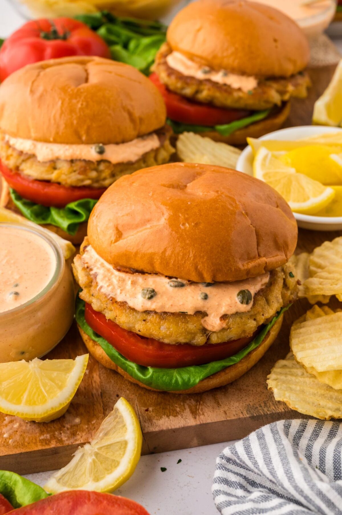 crab cake sandwiches with remoulade sauce, chips, and lemon on the side.