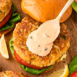 Crab cake sandwich with spoon pouring remoulade sauce on top.