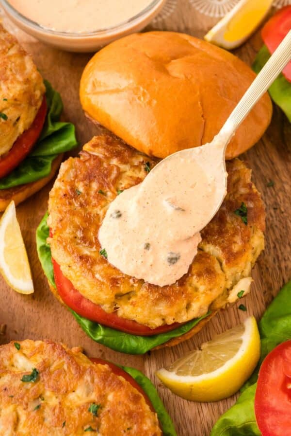 Crab cake sandwich with spoon pouring remoulade sauce on top.