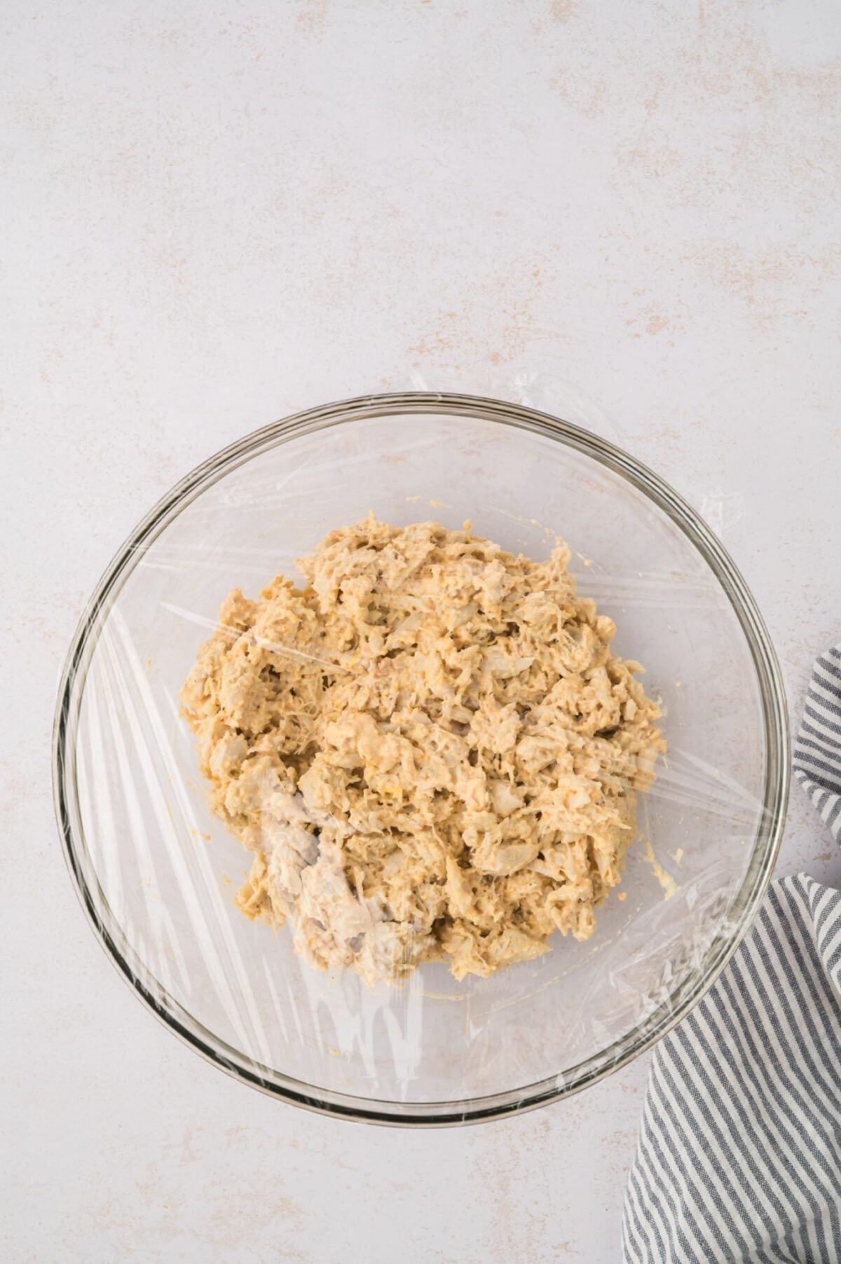 Crab cake mixture in a glass bowl with plastic wrap on top.
