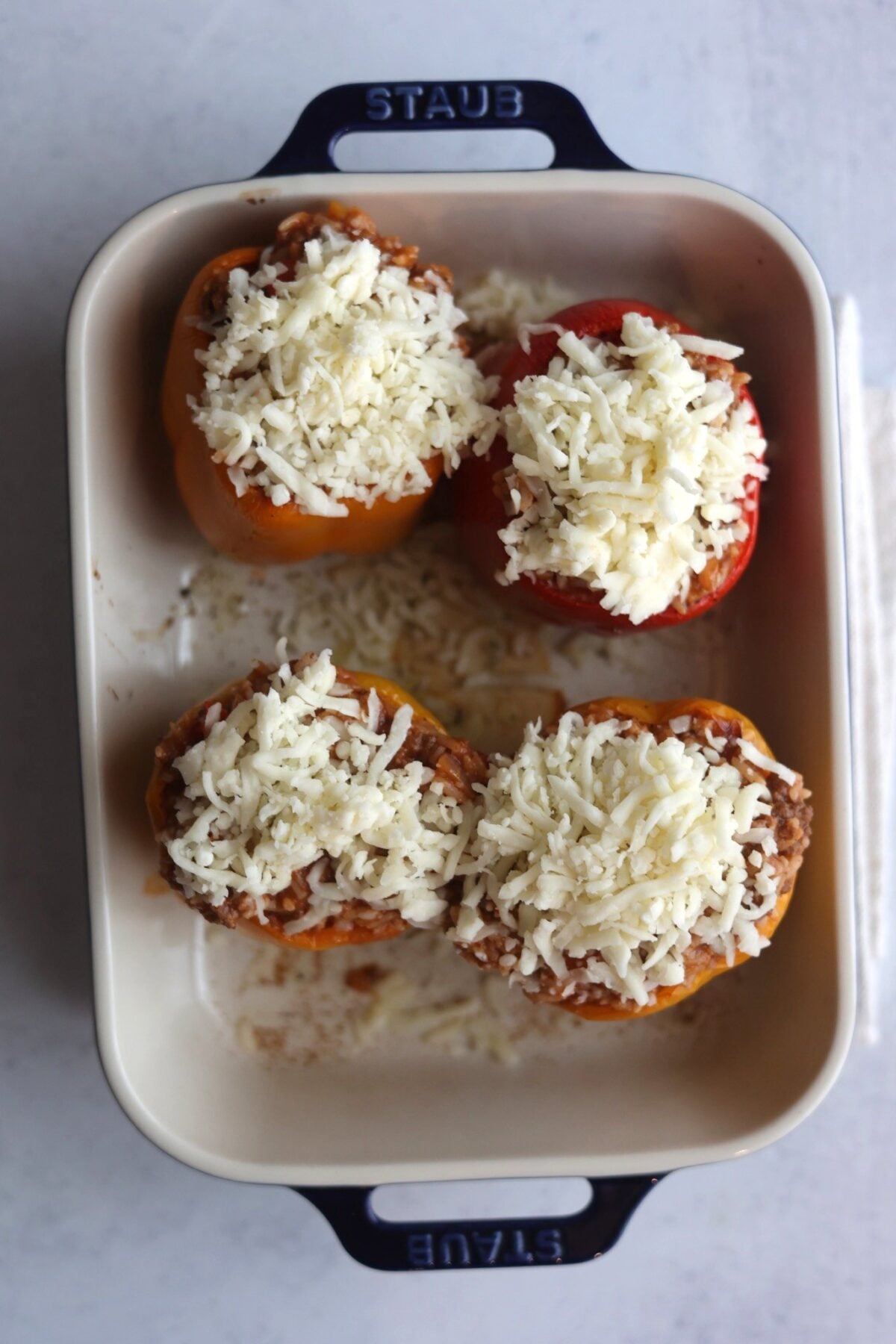 four stuffed peppers with shredded white cheese on top.