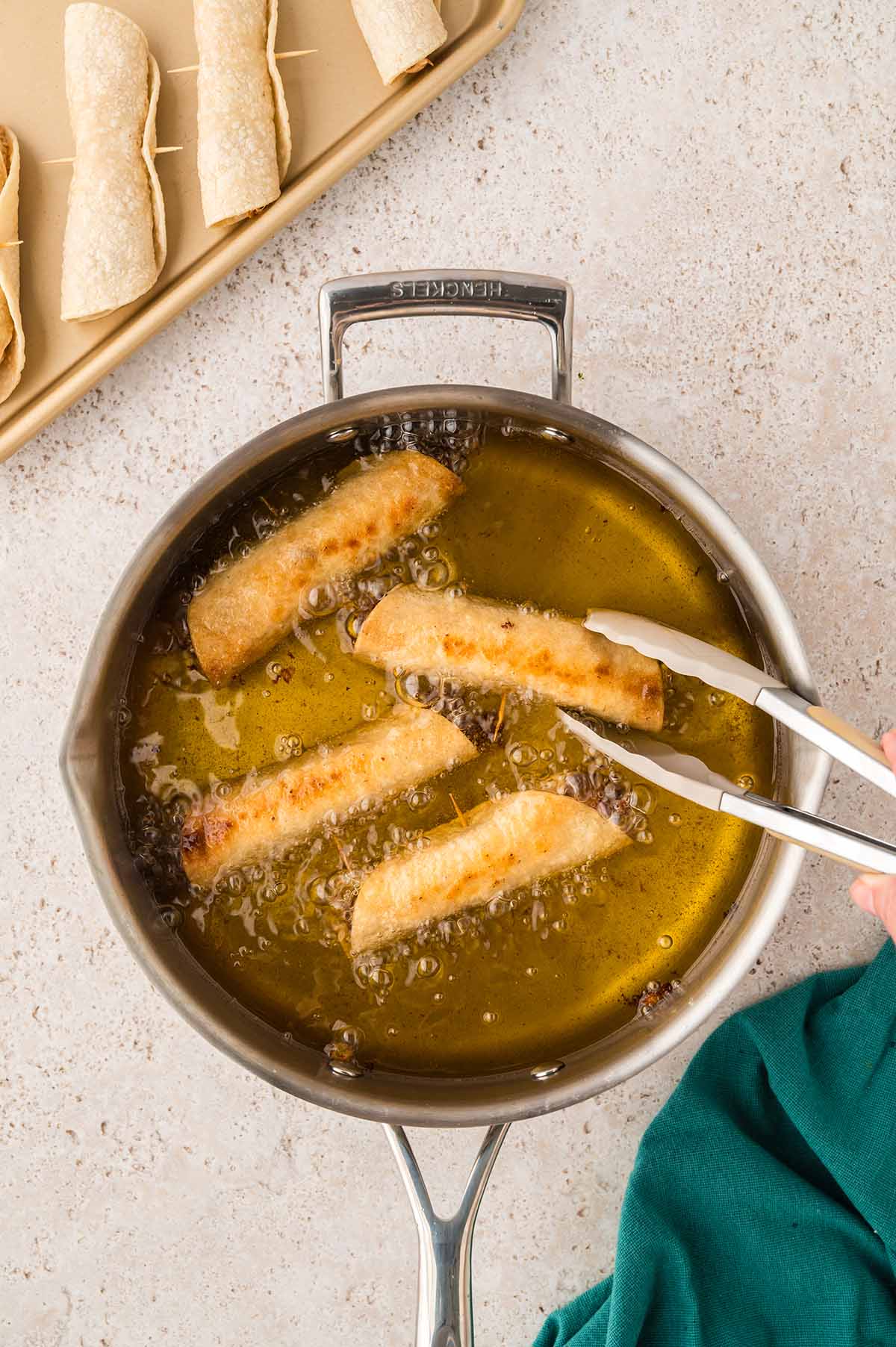 chicken flautas frying in a skillet with a tong.