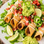 Chicken flautas on a plate with guacamole, pico de Gallo, jalapeños, and lime wedges,