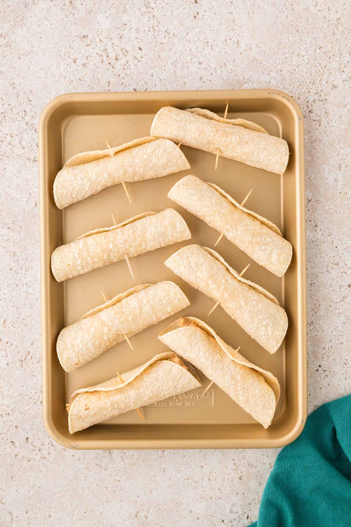 rolled tortillas with toothpicks on a baking sheet.